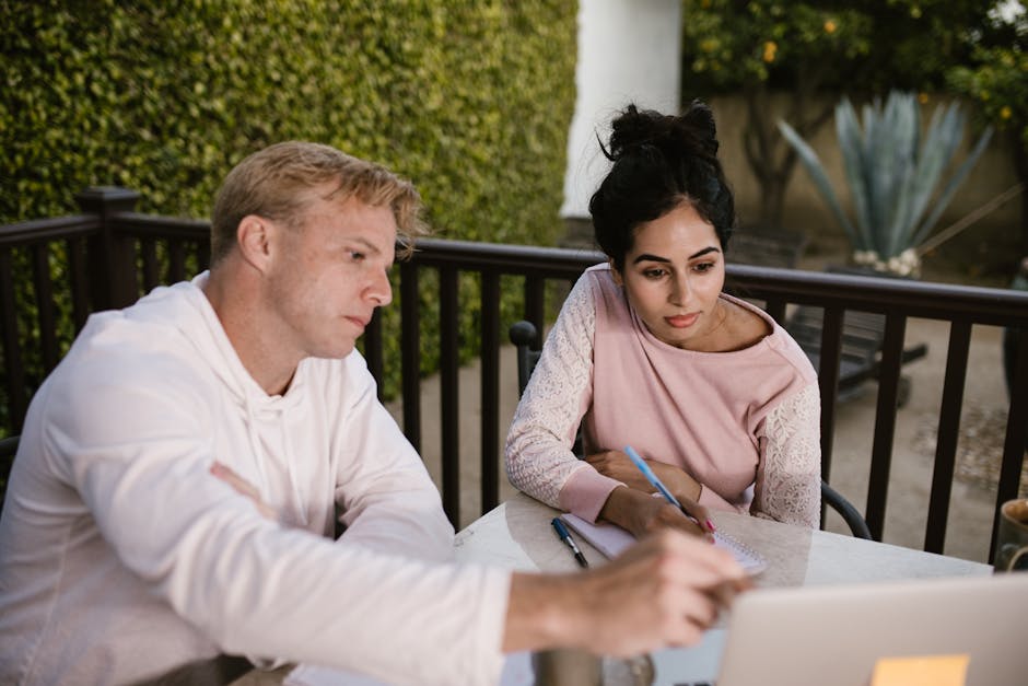 A man and woman engaged in online learning outdoors, collaborating on a laptop.