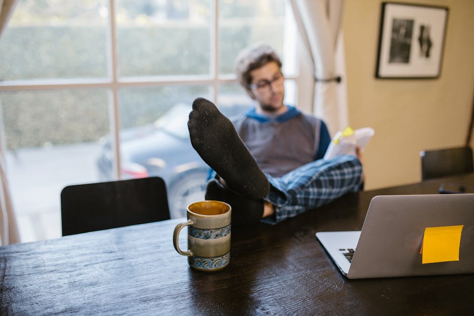 Relaxed home office scene with a person working remotely with laptop, coffee, and documents.